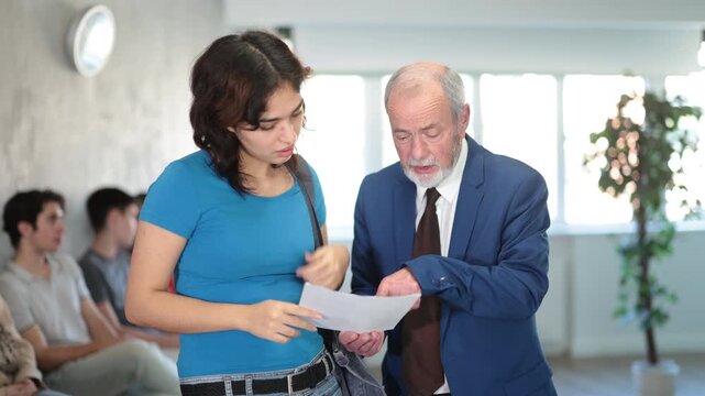 Serious senior manager talking with young girl concerning documents while standing in reception area. High quality 4k footage