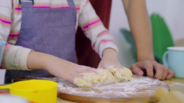 Asian girl kneading dough with flour on wooden board with parents assisting.