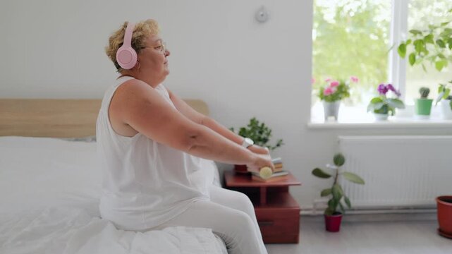 Back view of senior woman lifting yellow dumbbells overhead at home fitness at home