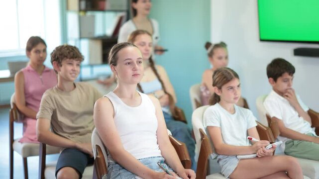 During lecture meeting at class, teens and preteens pupil listen to female teacher. Off-line training about application of AI courses, students listen to lecturer 