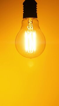 Electric light bulb switching on instantly against a yellow background with copy space