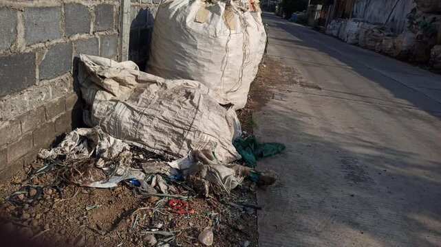 Large sacks filled with recyclable scrap materials placed beside a roadside area, reflecting waste collection and recycling activities in an urban environment