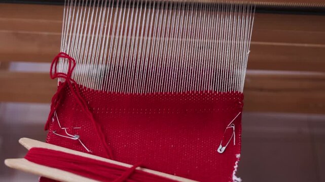 Close-up of red yarn woven into fabric on a traditional handloom. Warp threads remain visible above the growing textile during handmade production.