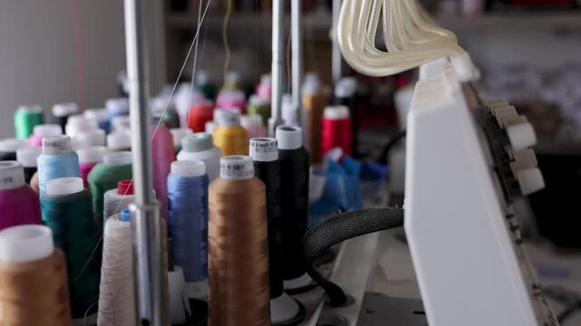 Close-up of colorful thread spools beside embroidery equipment in a textile workshop. Sewing materials used for traditional crafts, garment making, and fabric production.