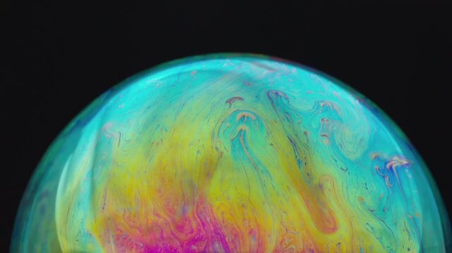 The abstract beauty of a hemispherical soap bubble surface, showcasing the phenomenon of light interference that creates dynamic, swirling, iridescent color patterns&mdash;a blend of turquoise,