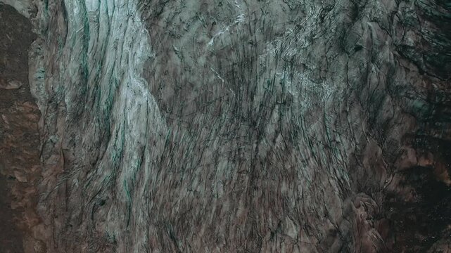 Visible features include natural crevasses, deep depressions, and a stunning blend of colors&mdash;snow-white, the gray of moraine rock, and the characteristic cyan-blue hues of perennial ice.