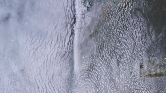 A frozen water surface featuring a unique pattern of ice cracks resembling scales or a spiderweb. 