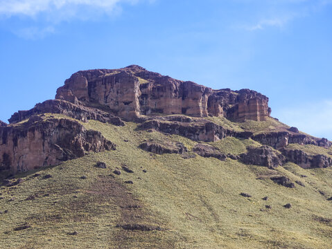 Red sedimentary rock mesa with eroded vertical walls on an Andean slope