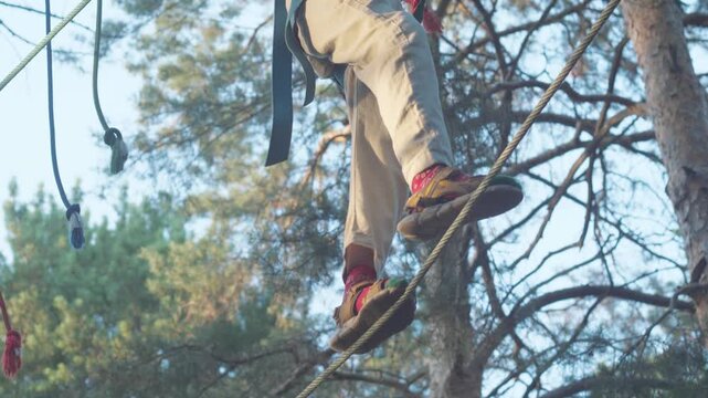 Close-up of the legs of a teenager carefully walking on a thin stretched rope at a height. The guy keeps his balance and passes a dangerous obstacle in an extreme rope park