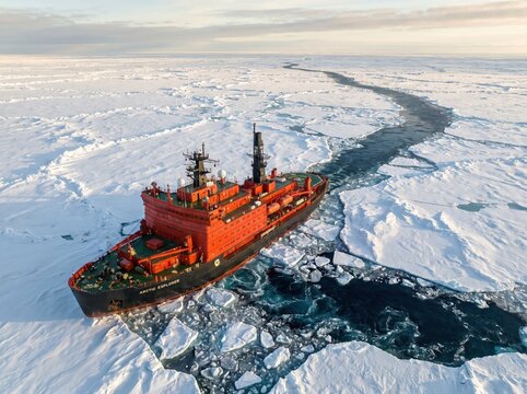 A heavy red icebreaker ship vessel sailing through the cold frozen ice of the arctic ocean sea during winter transportation.