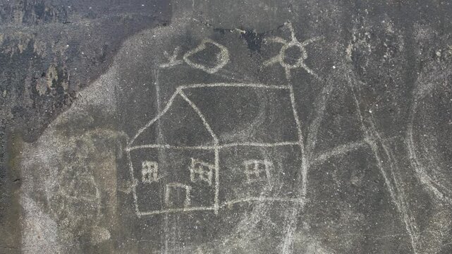 Child drawing scratched on dark dirty wall showing simple house sun tree and figure naive art street urban texture