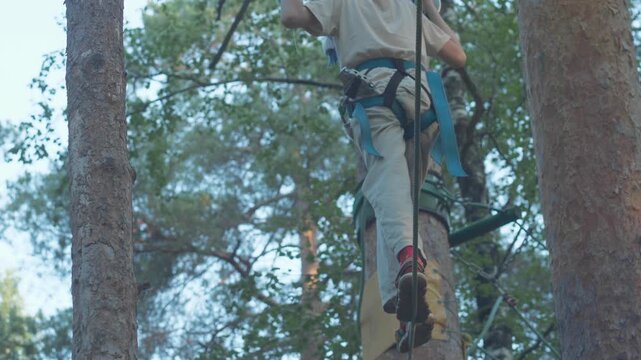 A teenager in climbing gear carefully walks along a stretched cable at a great height. The guy keeps his balance and holds onto a rope, overcoming an obstacle in a rope park.