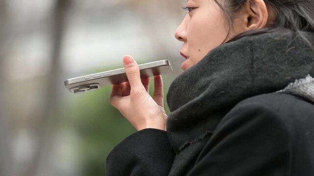 冬の屋外でスマートフォンのスピーカーホンを使う30代の日本人女性
