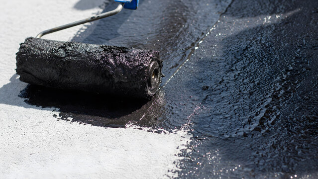 Applying black bitumen waterproof sealant with a paint roller on concrete