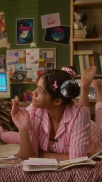 Vertical video of African American teenage girl in pyjamas lying down on bed and writing in notebook, thinking and smiling. Footage is ideal for storytelling about mental wellbeing or education