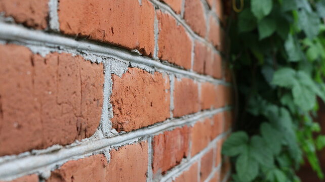 A textured red brick wall with crisp, angled gray cement joints. The rough texture of the blocks is visible in the foreground, while the right side of the frame fades into blur where green ivy leaves 