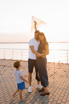 Happy Family With Child Flying Kite At Sunset