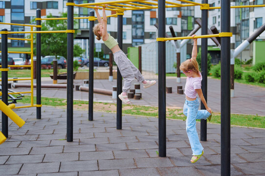 Two energetic girls enjoy swinging on the monkey bars at a modern outdoor playground