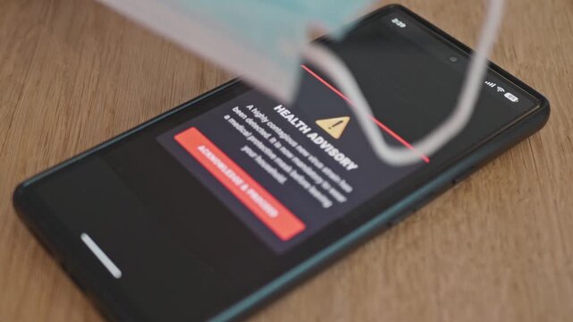 An epidemic warning on a smartphone screen, a person puts down a medical mask to avoid forgetting it before leaving home