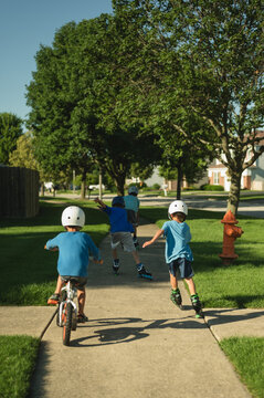Children riding bikes and rollerblades on suburban sidewalk