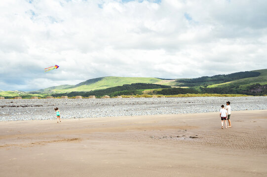 Family flying a colorful kite on a wide sandy beach