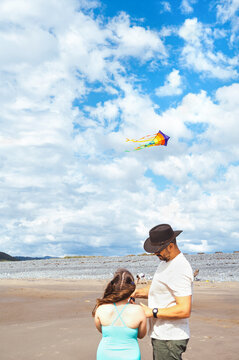 Father helping his daughter fly a colorful kite on the beach