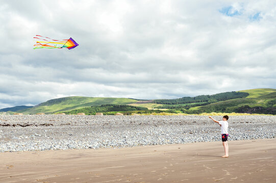 Child flying a colorful kite on a sandy beach