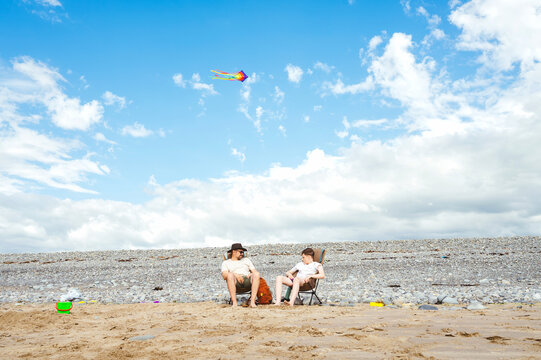 Father and teenager relaxing in camping chairs on a sandy beach