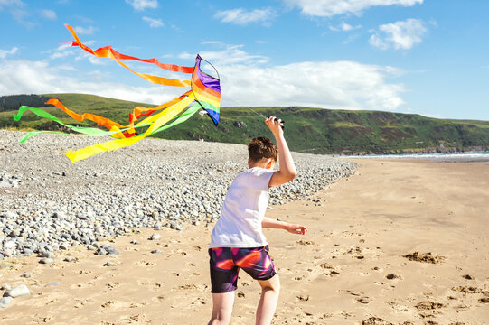 Teen boy running with a colorful kite on the beach