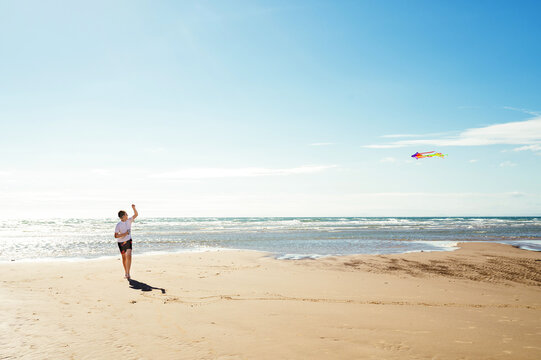 Teenager flying a colorful kite on a wide sandy beach