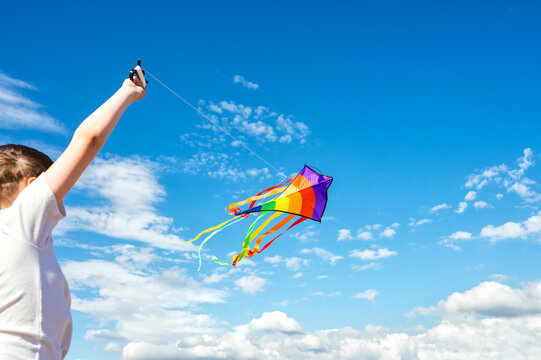 Teen boy flying a colorful kite beneath a blue sky