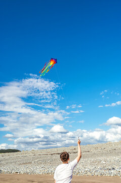 Teen boy flying a colorful kite beneath a blue sky