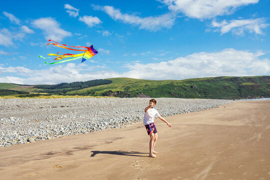 Teen boy flying a colorful kite on a sandy beach