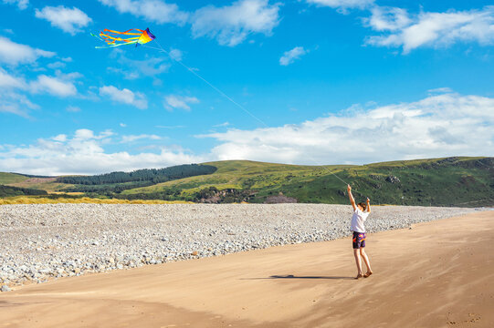 Teen boy flying a colorful kite on a quiet beach