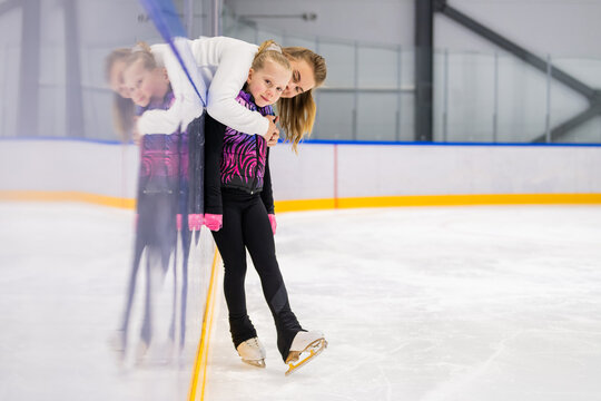 Coach hugging young figure skater on ice rink