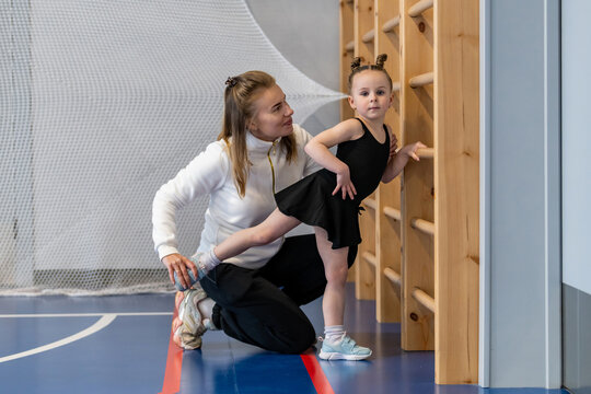 Gymnastics coach helps a little girl stretch