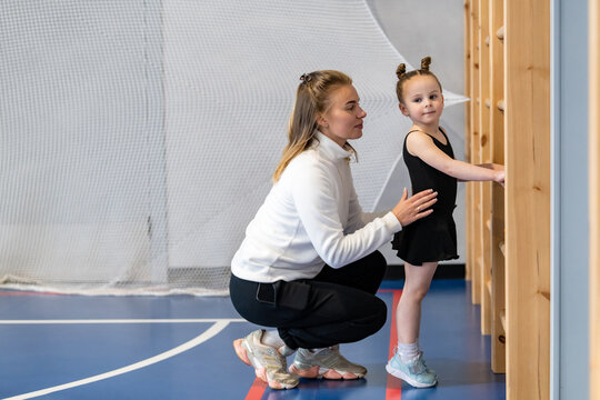 Female coach guides young girl during gym practice