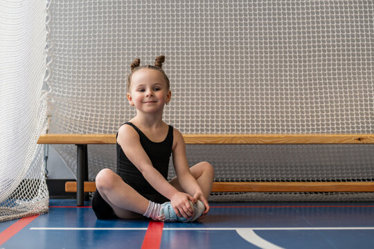 Little gymnast with space buns stretching in gym