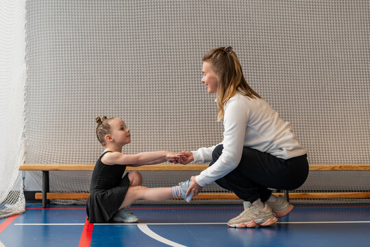 woman helps a little girl with balance exercises in a gym.