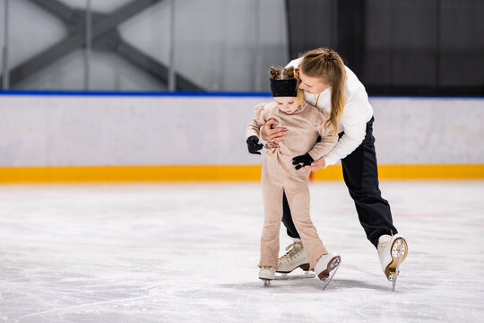 Woman helps a little girl learn to ice skate