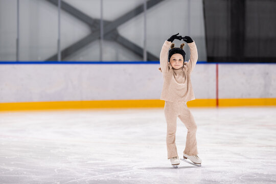 Little girl poses with her arms up on an ice rink