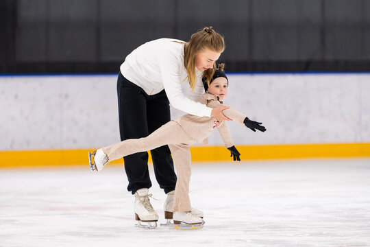 Figure skating coach teaches young girl on ice
