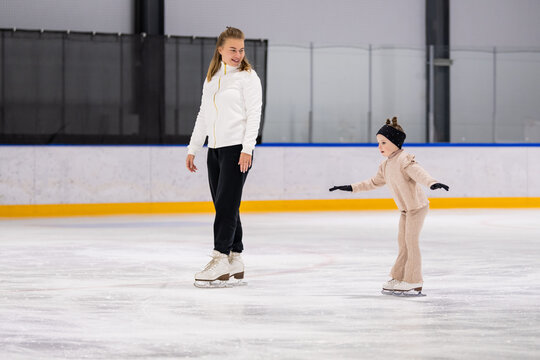 A female coach teaches a little girl ice skating