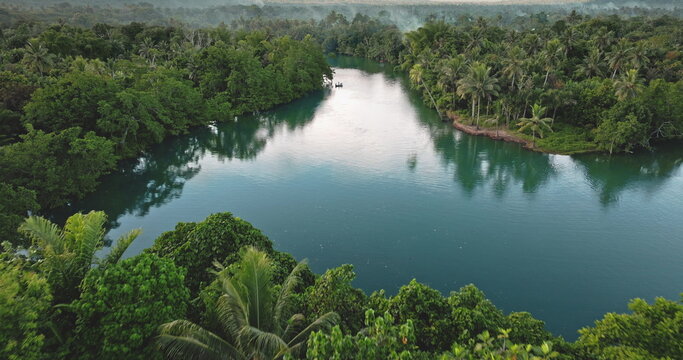 Luganville river winding through dense tropical rainforest on Santo, Vanuatu, with lush palms and thick green foliage, calm blue waters under cloudy sky, remote and serene. Aerial view drone flight