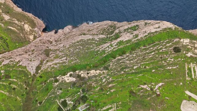 At the Dingli Cliffs in Malta, a drone captures the rugged coastline with rocky formations, sparse vegetation and the surrounding Mediterranean Sea in a broad top-down view.