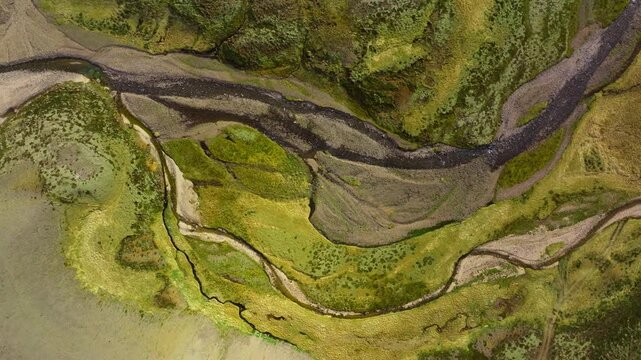 Meandering river in green mountain valley of Iceland, top down aerial