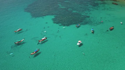 Traditional longtail boats and yacht floating on the clear turquoise tropical sea over visible coral reef, with people swimming and enjoying the vacation in Phuket, Thailand. Aerial view drone flight © Goinyk