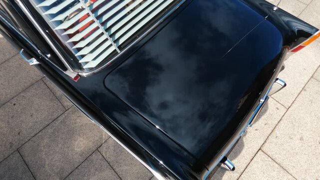 Overhead detail of a polished classic car trunk reflecting clouds and blue sky, rear shutters for shade