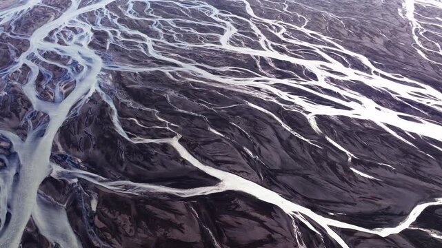 Drone shot of braided glacial river channels over black volcanic sand in Iceland. Complex braided glacial river delta weaving through dark volcanic plain.