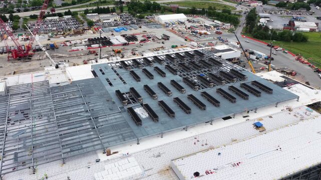 Data center in Lancaster shows partially installed rooftop cooling arrays on steel framework, red crawler crane, and construction staging areas below. Pennsylvania, USA. Aerial drone top down.
